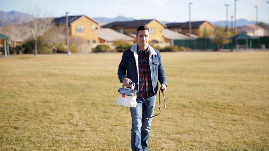 Man walking on lawn carrying a garden sprayer, residential houses in background