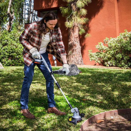 Man using electric grass trimmer on lawn in sunny residential garden setting.